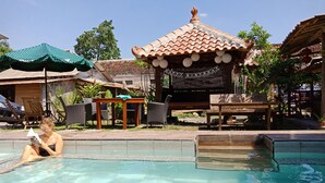 Un espace piscine doté d’une terrasse en bois, de chaises longues et d’un petit pavillon agrémenté d’une pancarte « Joyeux anniversaire ».