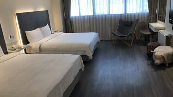 A hotel room with two beds, a desk, a chair, and a television.
