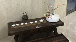 A wooden table with a white bowl and teapot, set against a tiled wall with hanging red lanterns.