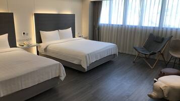 A hotel room with two beds, a desk with a phone, a chair, and a large window with curtains.
