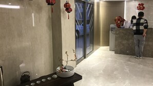 A reception area with a marble floor, a reception desk, a wall-mounted sign, and a decorative vase with flowers.