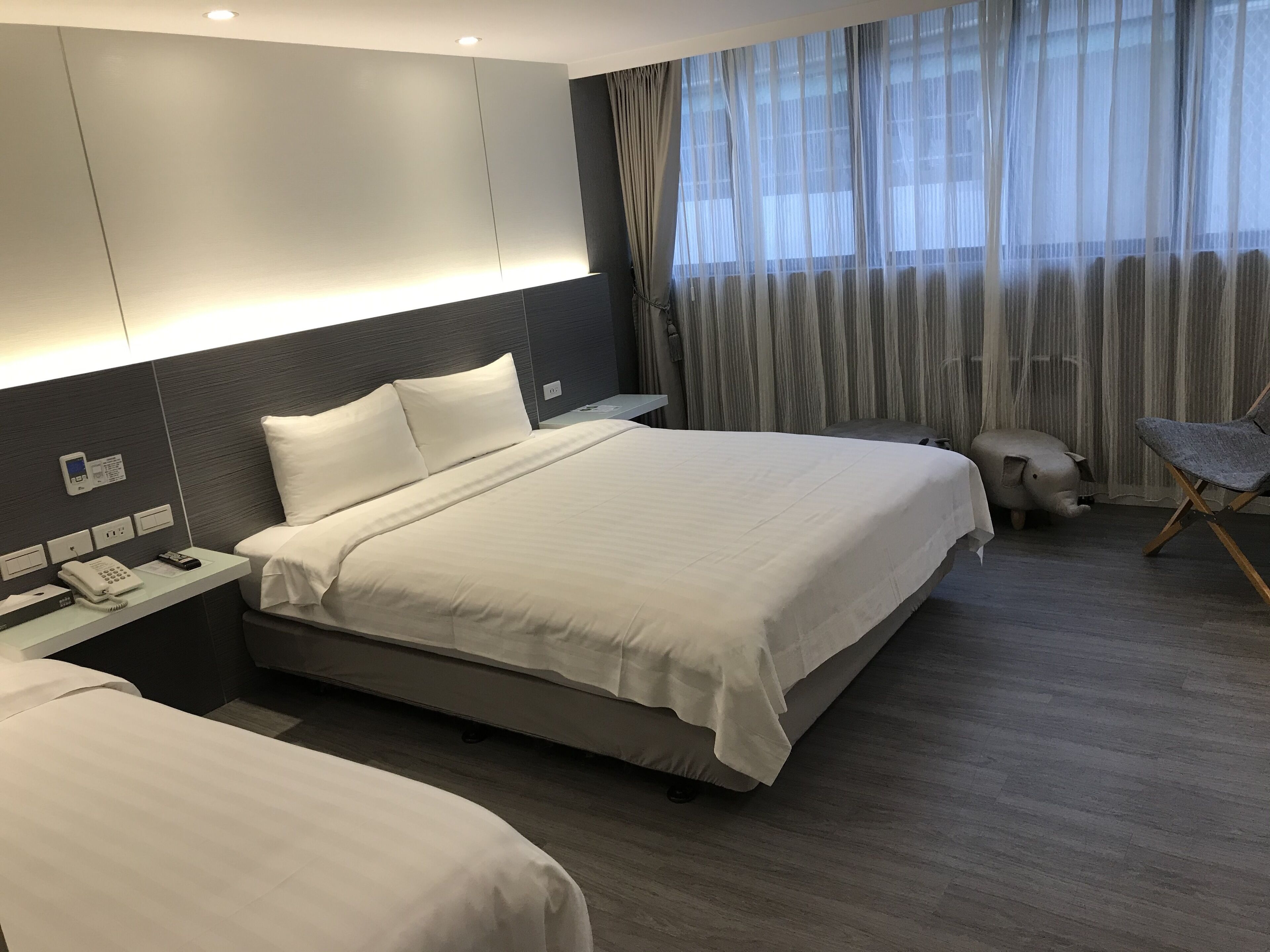 A modern hotel room with a large bed, bedside tables, a phone, and a chair.