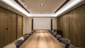 A conference room with a long wooden table, black chairs, and a projector screen.