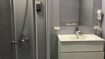 A modern bathroom with a glass-enclosed shower, a white sink with a mirror above it, and a hairdryer on the wall.