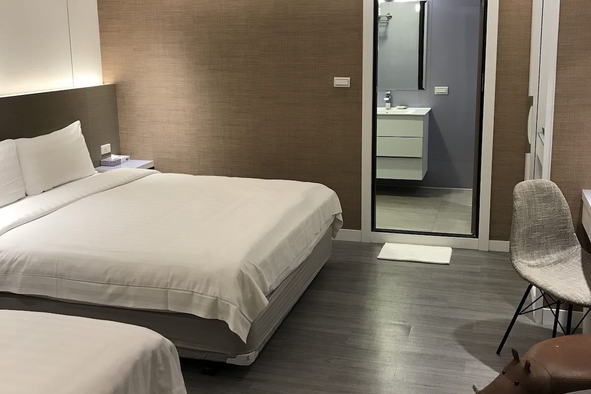 A modern hotel room with a large bed, a smaller bed, a chair, and a small table.