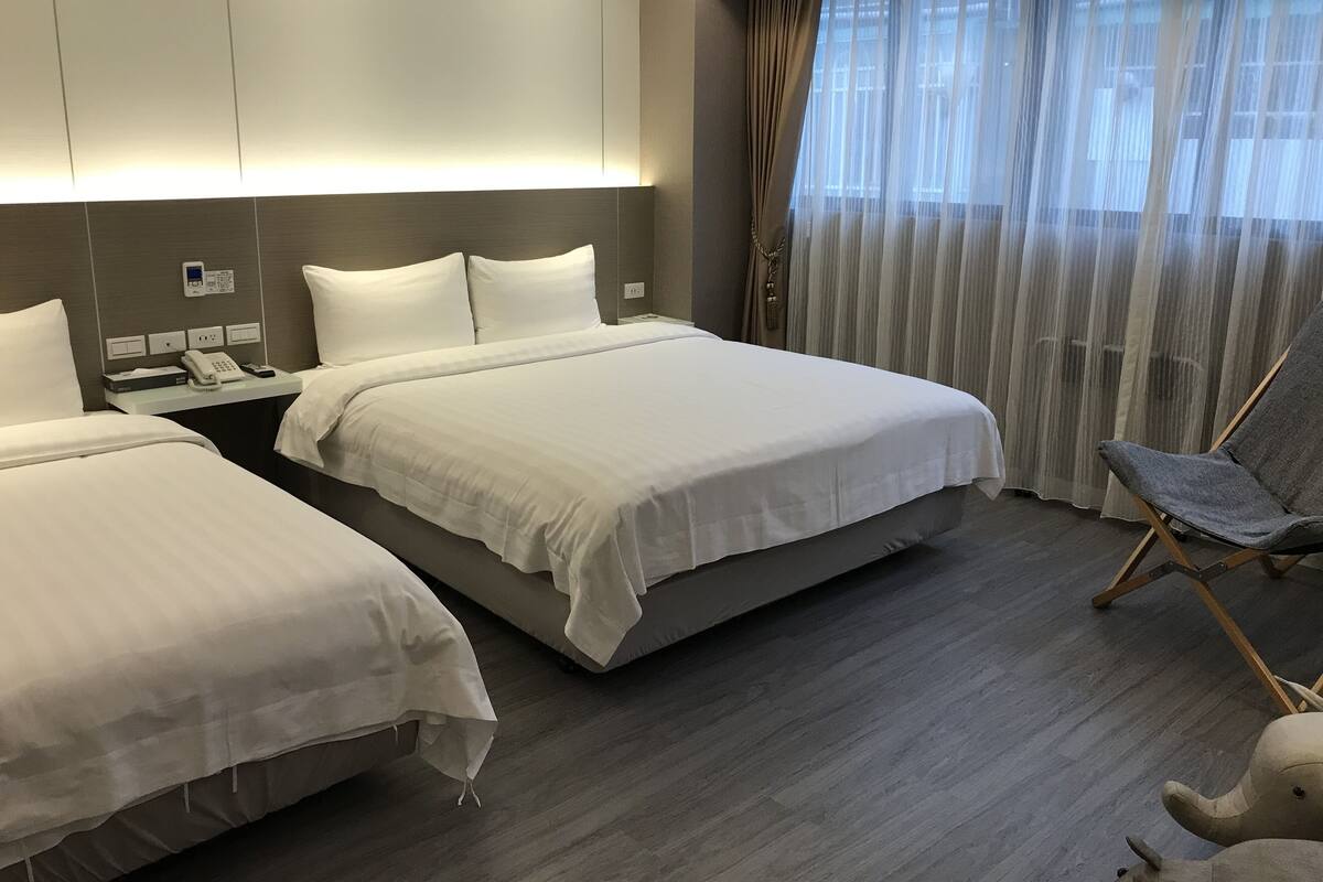 A hotel room with two beds, a desk with a phone, and a chair.