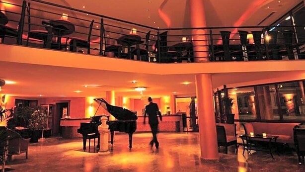 A spacious lobby with a grand piano, a reception desk, and a balcony with seating. - Hotel Santo (Karlsruhe)