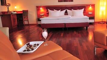 Ein Hotelzimmer mit einem großen Bett, zwei Nachttischlampen, Holzboden und einem kleinen Tisch mit einem Glas Wasser und Pralinen.