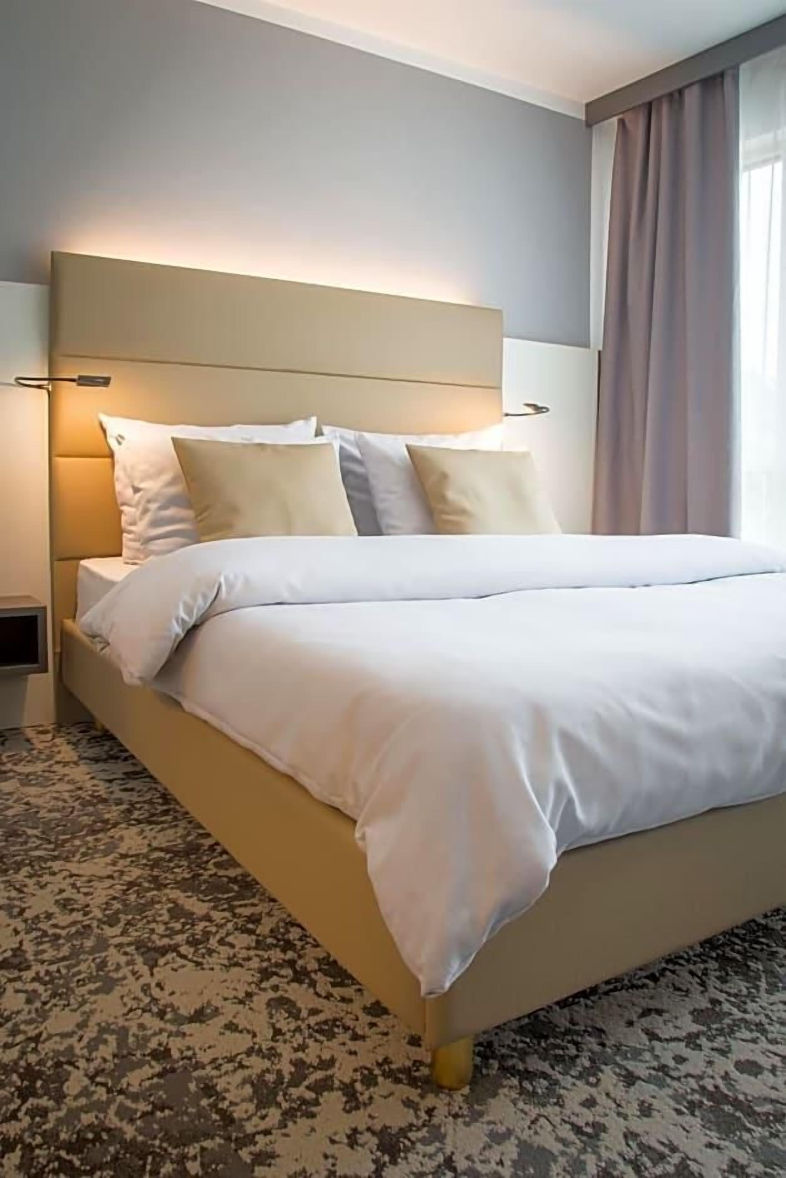 Habitación de hotel con una cama grande, cabecera con iluminación integrada, mesita de noche y alfombra estampada.