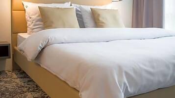 Quarto de hotel com cama grande, cabeceira com iluminação embutida, mesa de cabeceira e tapete estampado.