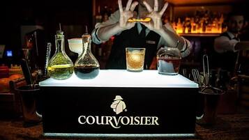 Uma área de bar com um letreiro 'COURVOISIER' e um bartender fazendo um truque.