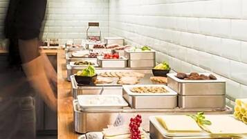 Disposição de buffet com diversos alimentos e uma pessoa servindo.