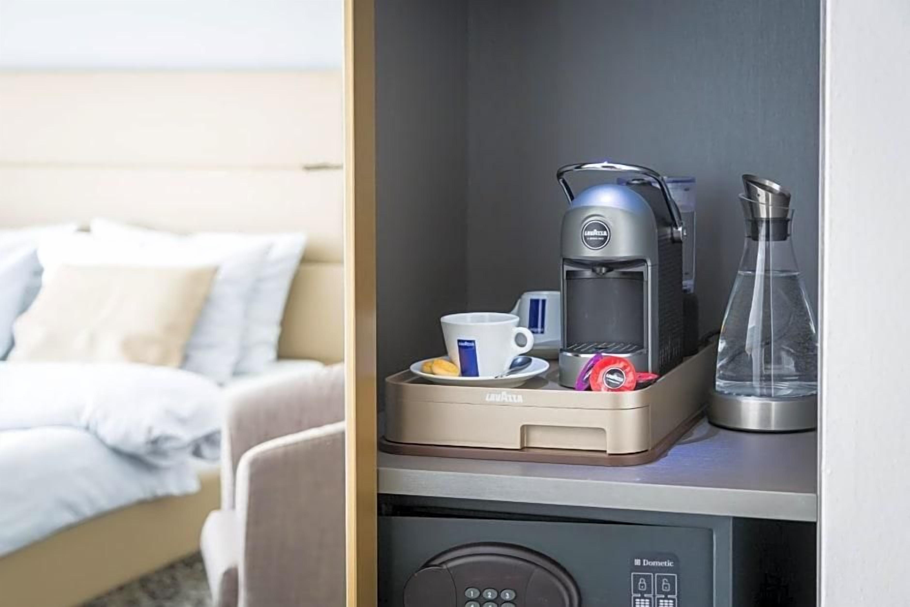 Quarto de hotel com cama, máquina de café, uma chávena e um copo sobre um balcão.