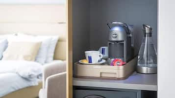 Quarto de hotel com cama, máquina de café, uma chávena e um copo sobre um balcão.