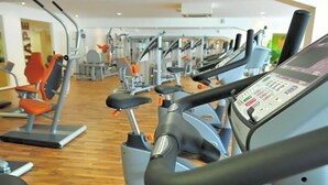 A gym with multiple exercise machines, including treadmills and weight machines, arranged in rows. - Hotel Santo (Karlsruhe)