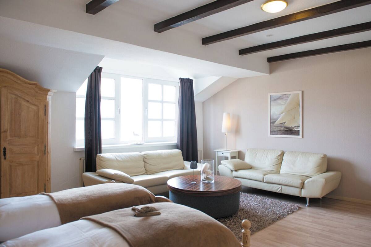 Un salon spacieux avec un plafond haut, une grande fenêtre avec des rideaux, un canapé, une table basse et une lampe.
