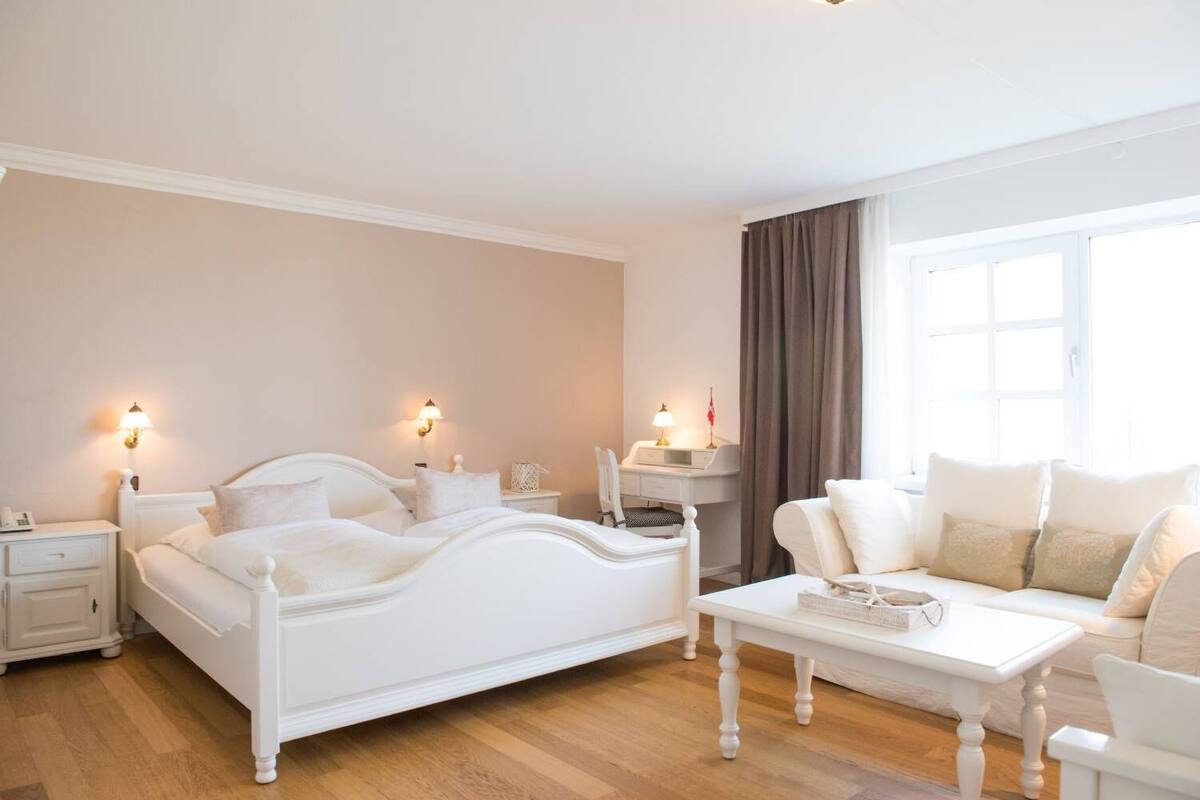 Une chambre à coucher avec un lit blanc, des tables de chevet, un bureau, une chaise et un canapé.