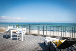 Une terrasse en bois avec une table et des chaises, donnant sur une plage et la mer.