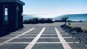 A paved pathway leading to a small building with a view of the ocean. - Strandhotel Lodge am Meer (Gluecksburg)