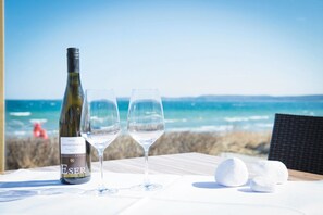 Une table avec une bouteille de vin et deux verres, placée devant un paysage de plage.