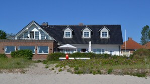 A two-story building with a black roof and white trim, featuring a large bay window and a balcony. - Strandhotel Lodge am Meer (Gluecksburg)