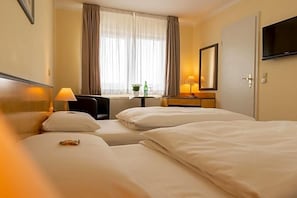 Une chambre d’hôtel avec deux lits, un bureau avec une chaise, une télévision et une fenêtre avec des rideaux.