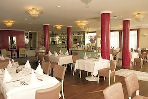 Un restaurant doté de nombreuses tables, de colonnes rouges et d’un espace bar.