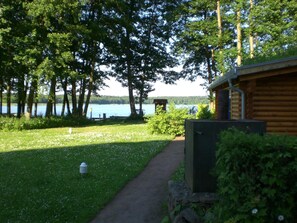 A wooden cabin with a pathway leading to a dock, surrounded by lush greenery and a lake.