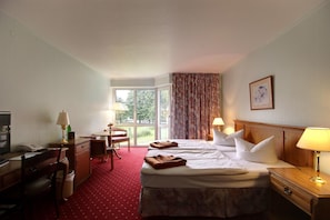 Habitación de hotel con cama, dos mesitas de noche, un escritorio con silla, teléfono y ventana con cortinas.