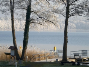 Un parque junto al lago con bancos, un comedero para pájaros y una barandilla metálica a lo largo del camino.