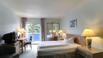 Ein Hotelzimmer mit einem Bett, einem Schreibtisch mit Fernseher, einem Sessel und einem Fenster mit Vorhängen.