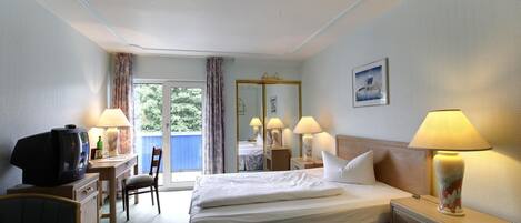 Habitación de hotel con cama, escritorio con televisor, una silla y ventana con cortinas.
