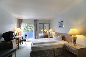 Habitación de hotel con cama, escritorio con televisor, una silla y ventana con cortinas.