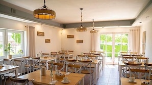 Un comedor amplio con varias mesas y sillas, ventanas grandes y lámparas colgantes.