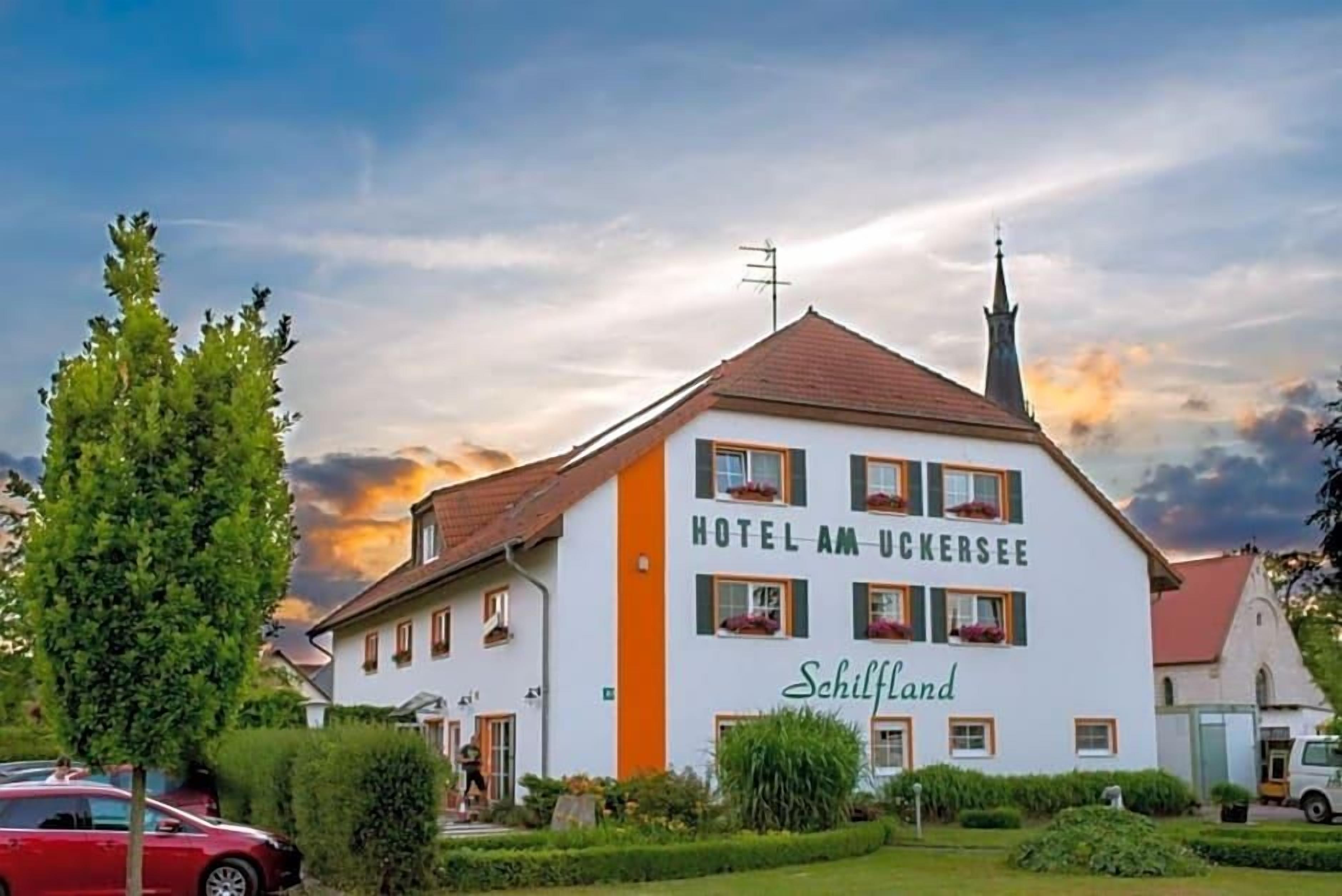 Un edificio bianco con il cartello 'HOTEL AM UCKERSSEE' e la scritta 'Schilfland'.