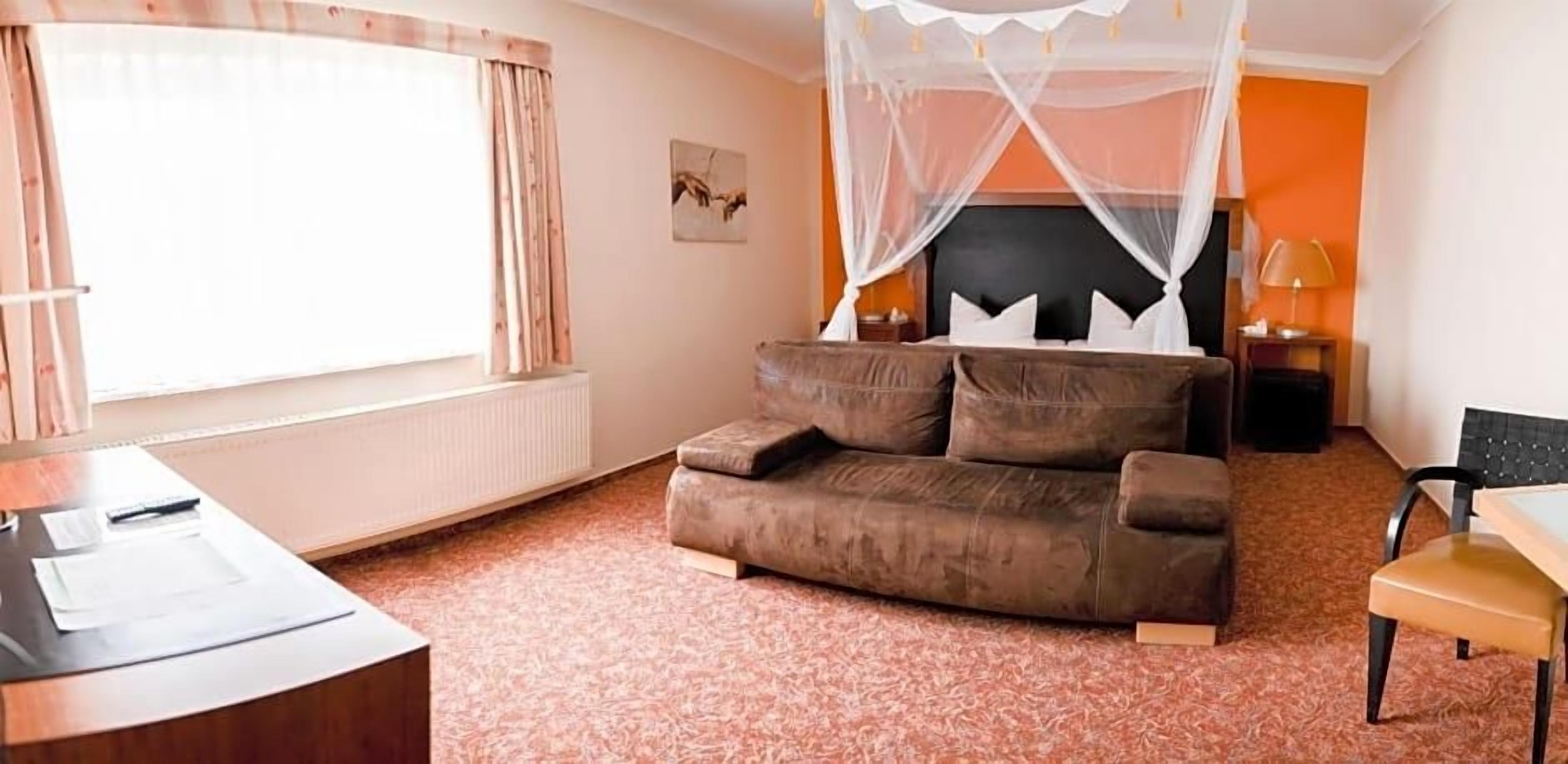 Ein Zimmer mit Bett, Schreibtisch, Stuhl, einem Fenster mit Vorhängen und einem Wandbild.