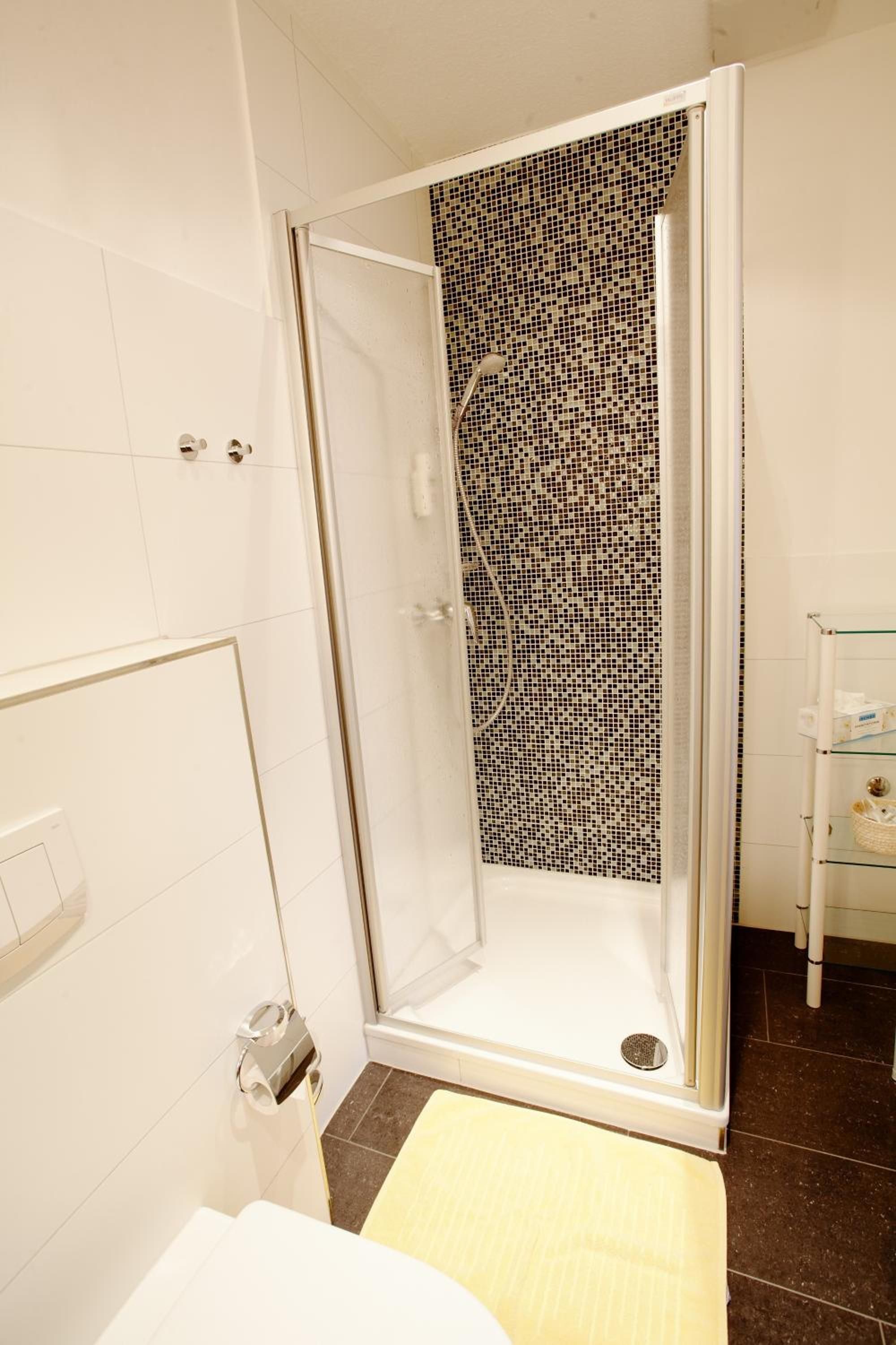 A shower with a glass door and a mosaic tile wall.