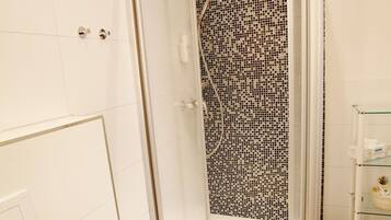 A shower with a glass door and a mosaic tile wall.