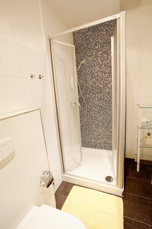 A shower with a glass door and a mosaic tile wall.