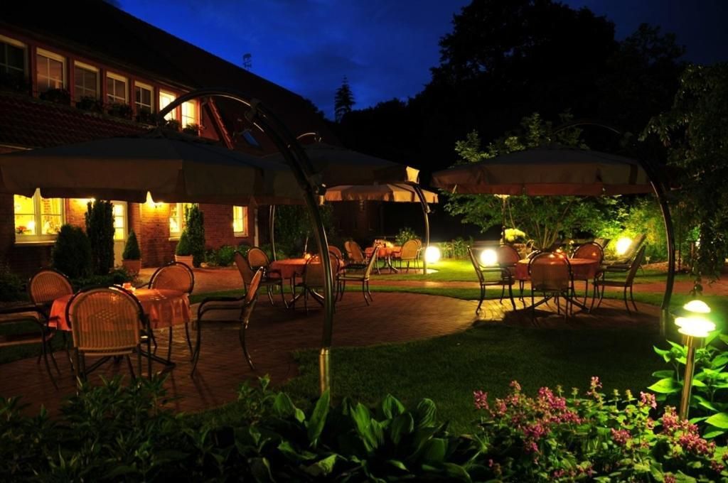 An outdoor patio area with tables and chairs under umbrellas, surrounded by greenery.