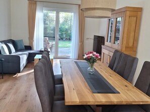 A modern living room with a sofa, a dining table with chairs, a fireplace, and a view through a glass door.