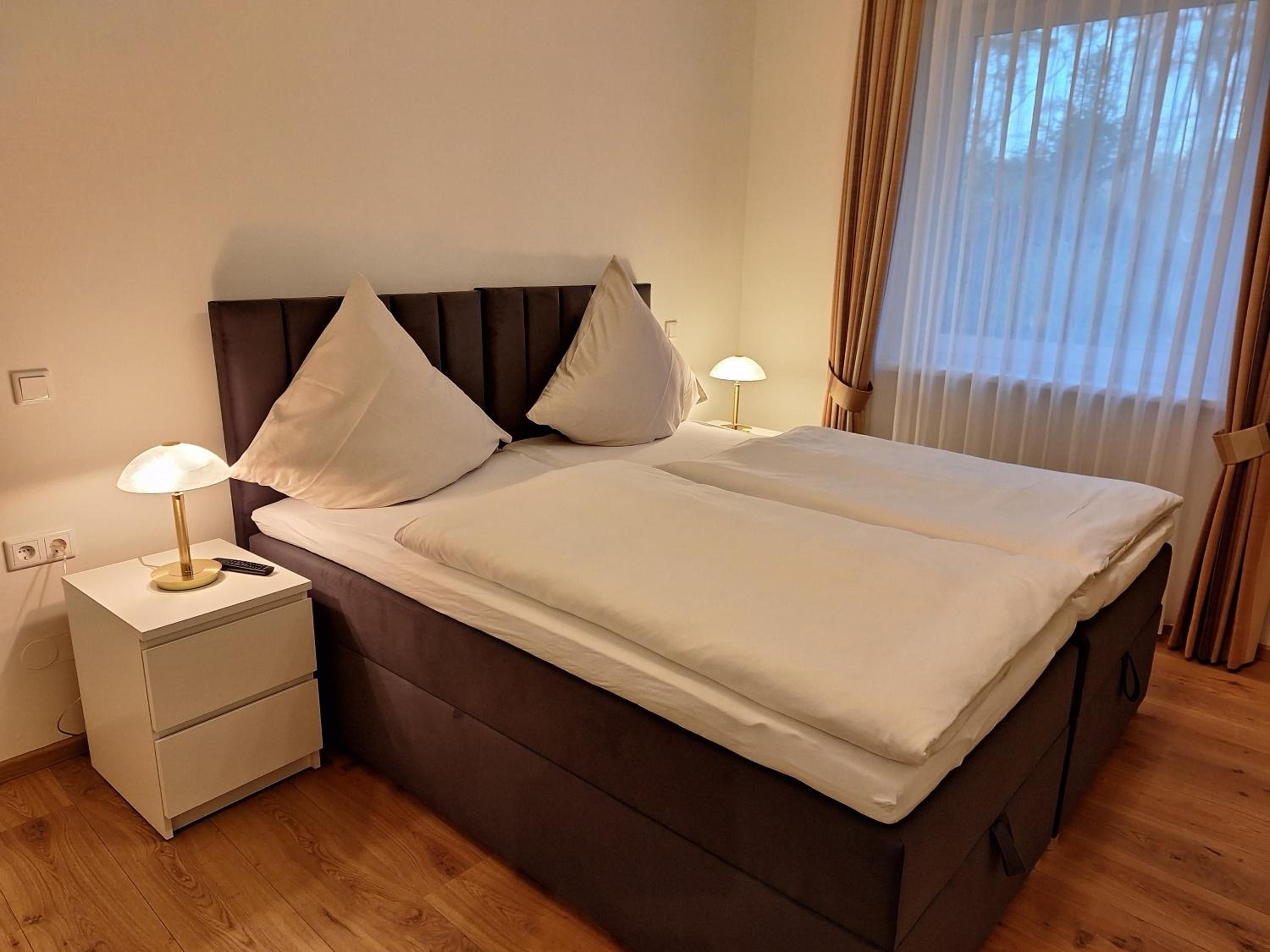 A neatly made bed with white linens, a brown headboard, and two bedside lamps.