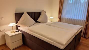 A neatly made bed with white linens, a brown headboard, and two bedside lamps.