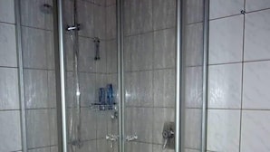 Une cabine de douche fermée par des parois en verre, dotée d’un pommeau de douche à main et d’un robinet fixé au mur.