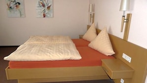 Un lit simple avec un matelas, des oreillers et une tête de lit, dans une pièce dont le sol est recouvert d’une moquette.