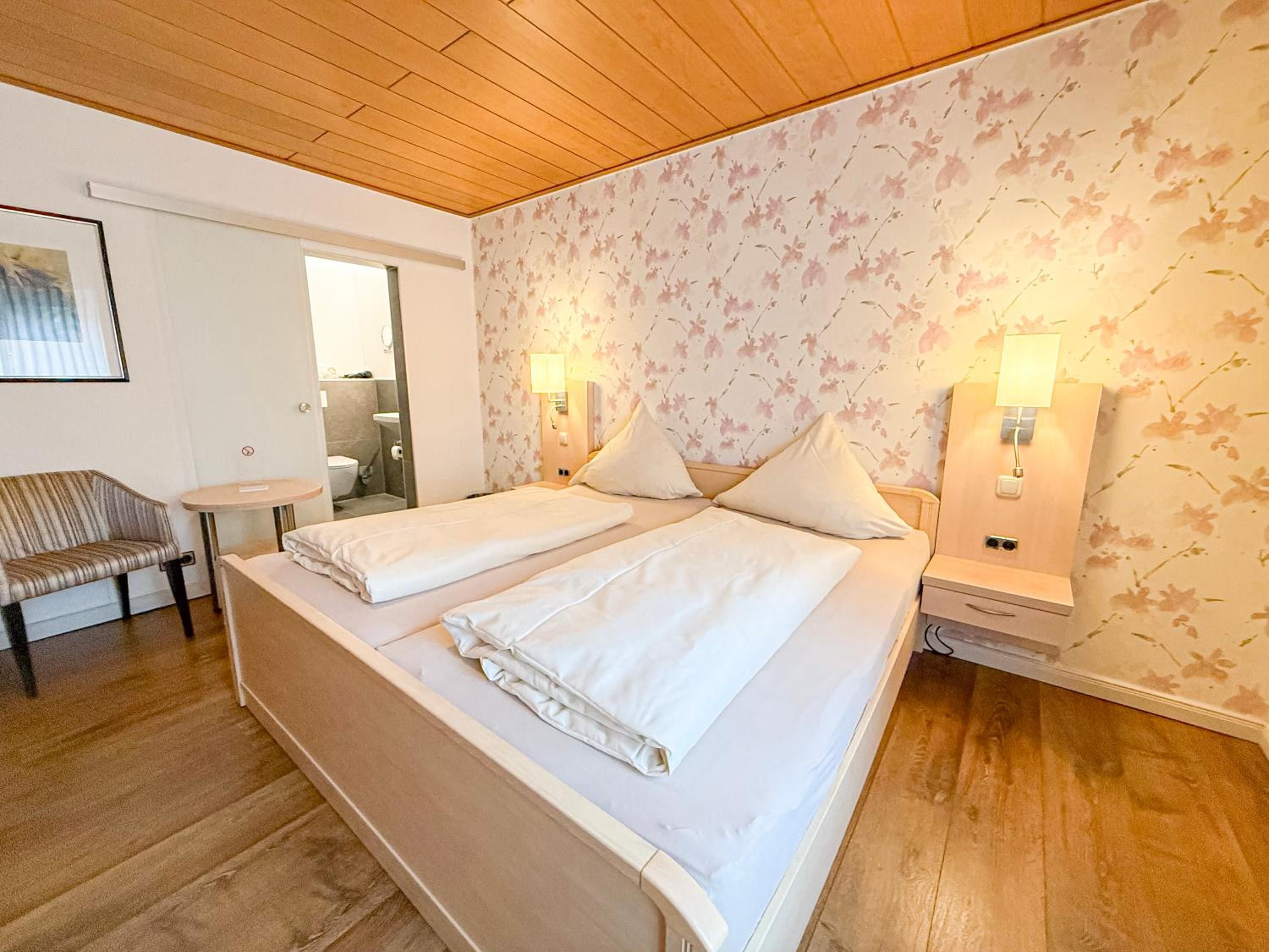 A double bed with two pillows, a bedside table, a chair, and a bathroom visible through an open door.