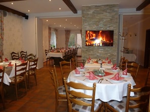 A dining area with multiple tables set for a meal, a fireplace, and a television screen displaying a fire.