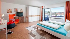 Ein modernes Hotelzimmer mit Bett, Fernseher, Sessel und Blick auf die Stadt.