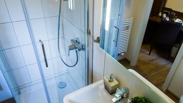 Ein modernes Badezimmer mit Duschkabine aus Glas, einem weißen Waschbecken mit einer kleinen Pflanze und einem sichtbaren Handtuchhalter.