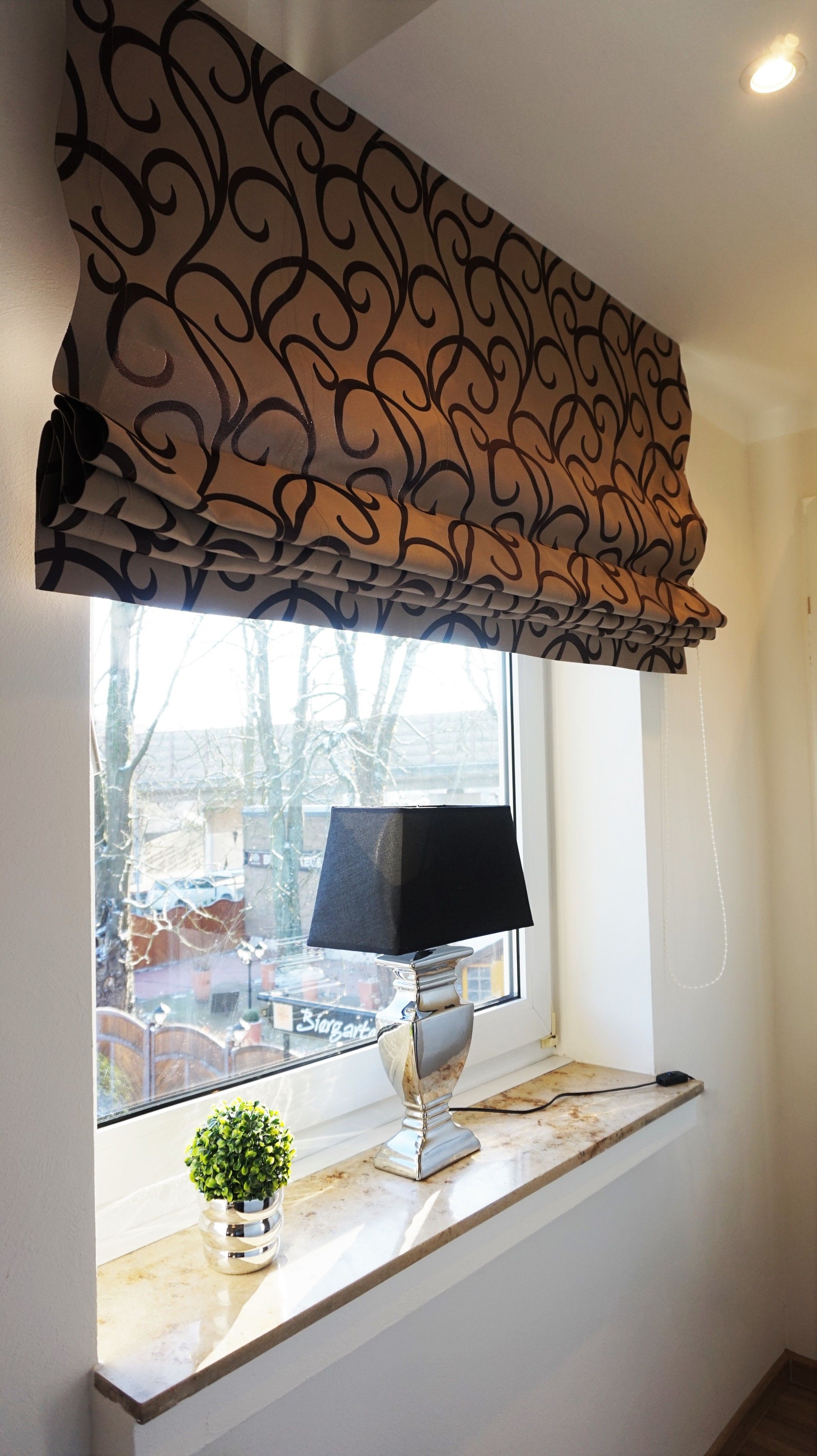 A window with a decorative valance, a table lamp, and a small potted plant on a marble ledge.